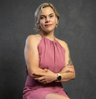 #ParaCegoVer: Foto de perfil de Dan&uacute;bia Don&aacute;, Consultora de Beleza Independente Mary Kay. Mulher de cabelos loiros curtos, usando vestido rosa com decote halter, bra&ccedil;os cruzados e express&atilde;o confiante. Fundo cinza escuro.